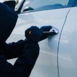 Zlodej v kukle sa pokúša vlámať do auta – dôležitosť ochrany vozidla pred krádežou.