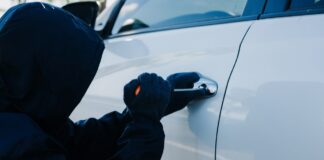 Zlodej v kukle sa pokúša vlámať do auta – dôležitosť ochrany vozidla pred krádežou.