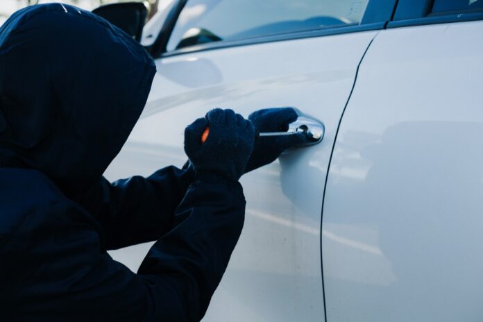 Zlodej v kukle sa pokúša vlámať do auta – dôležitosť ochrany vozidla pred krádežou.