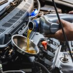 Automechanik nalieva motorový olej do motora pri bežnej údržbe v autoservise.