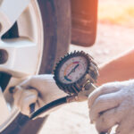 Vodič meria tlak v pneumatikách pomocou tlakomeru pri stojacom aute.