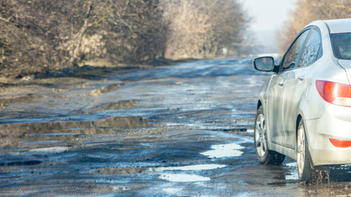 Koleso auta prechádzajúce cez hlboký výtlk na rozbitej ceste, ilustrujúce riziko poškodenia podvozku a pneumatiky.